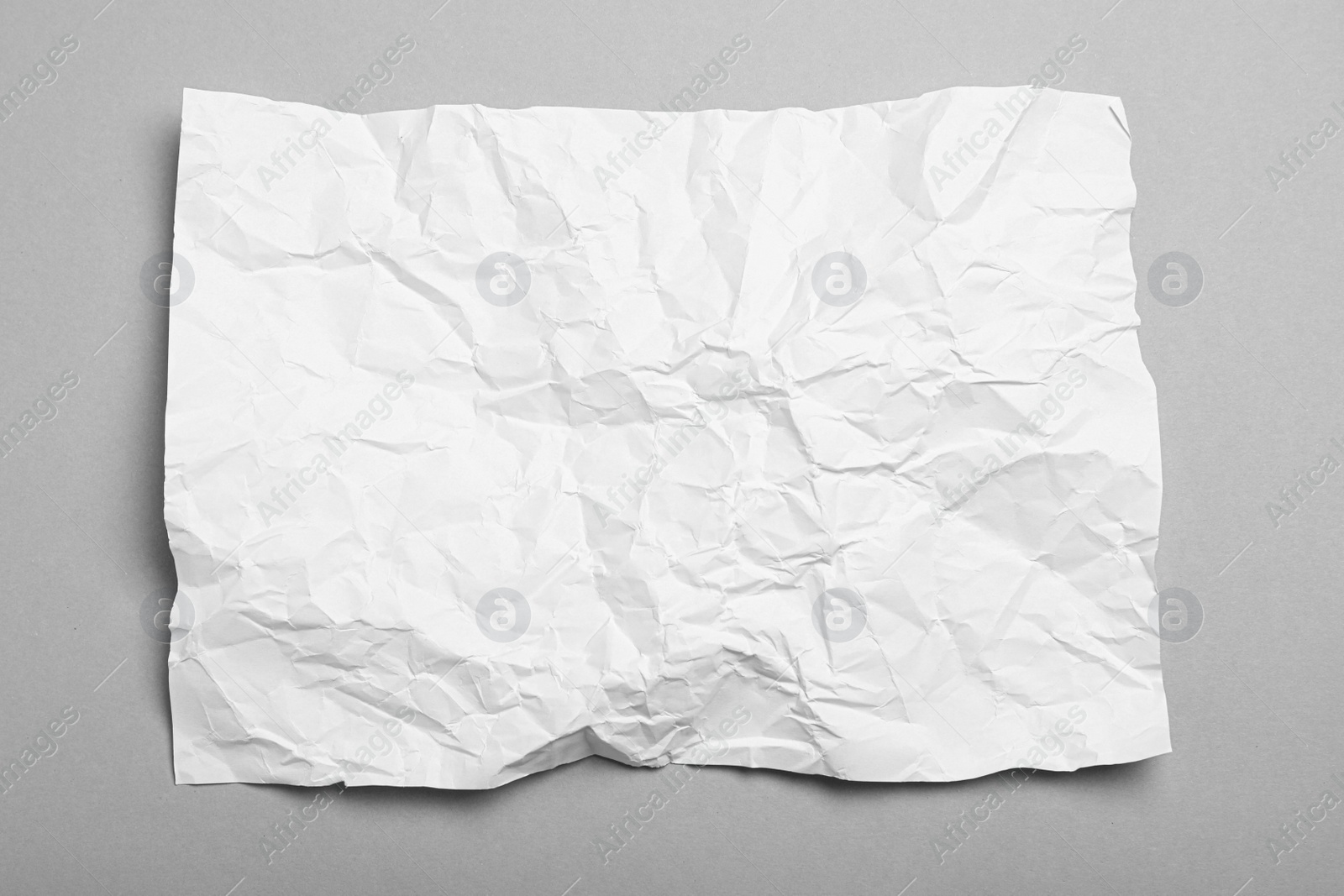 Photo of Sheet of white crumpled paper on grey background, top view