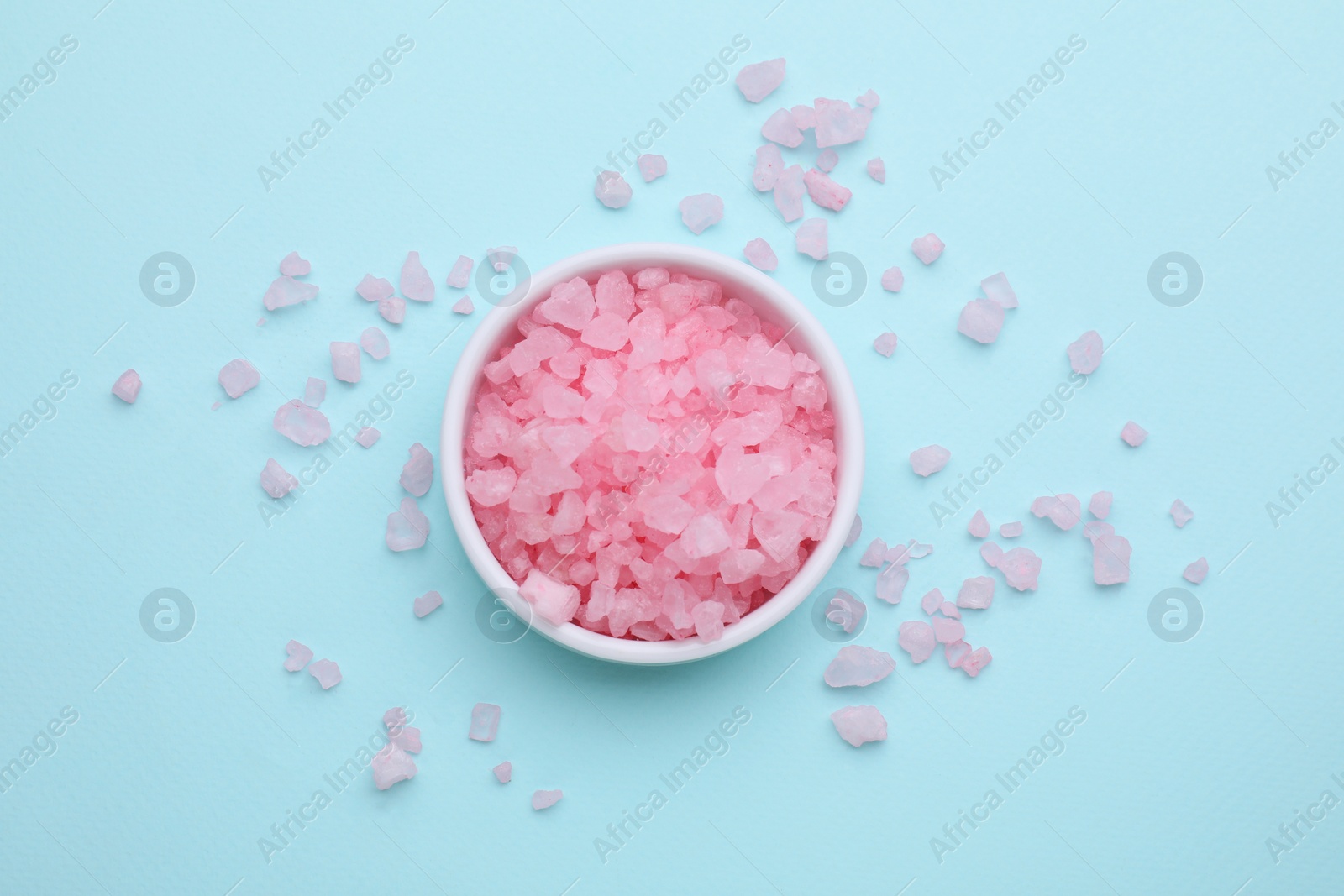 Photo of Bowl with pink sea salt on light blue background, top view