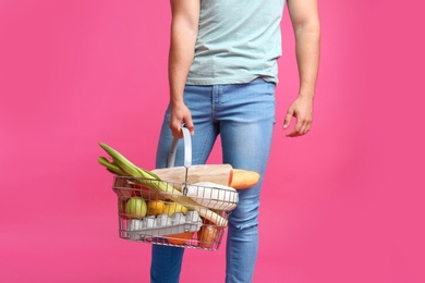 Photo of Young man with shopping basket full of products on pink background, closeup