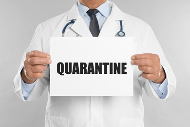 Image of Doctor holding sign with text QUARANTINE on light grey background, closeup. Stay at home during coronavirus outbreak