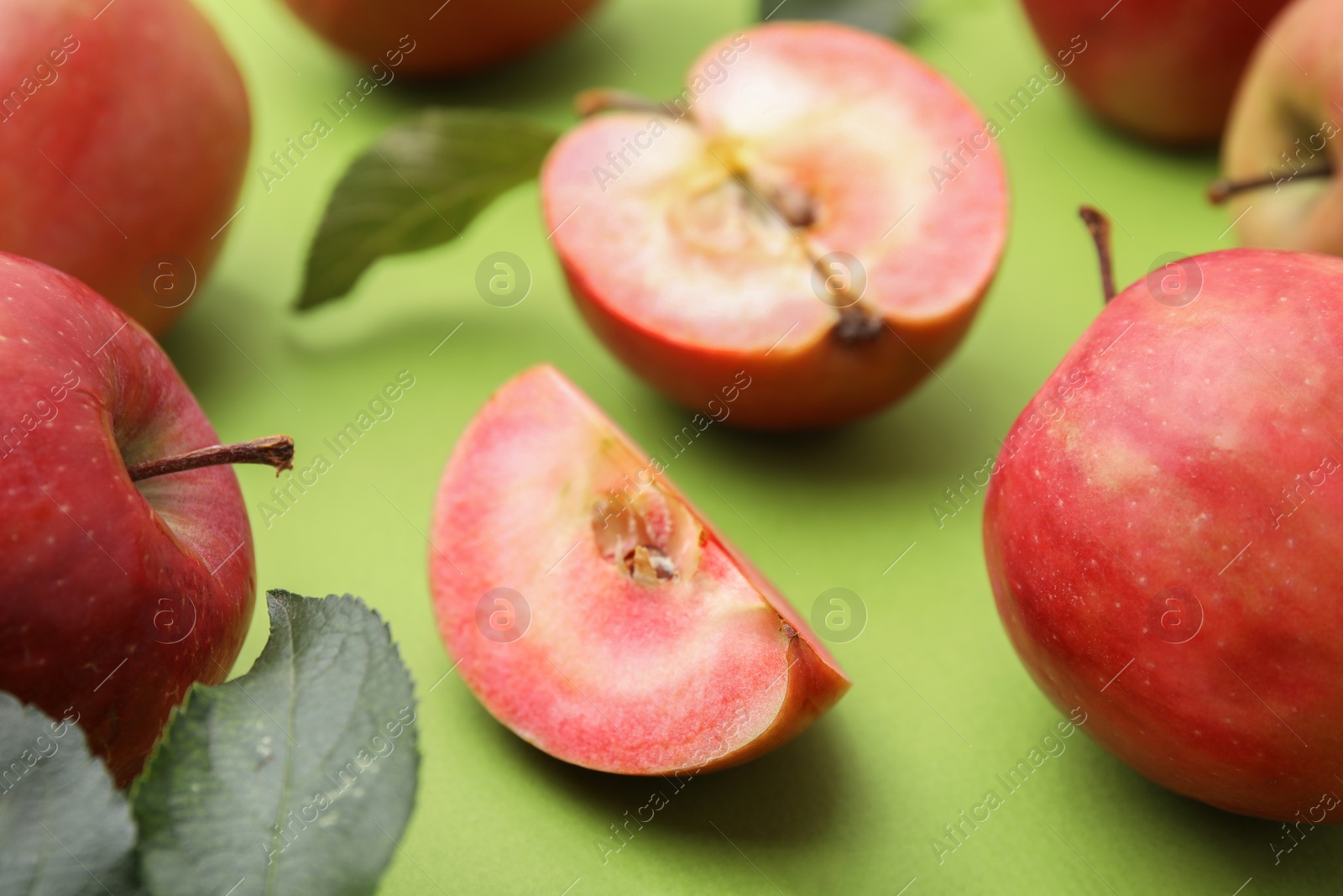 Photo of Tasty apples with red pulp and leaves on light green background, closeup