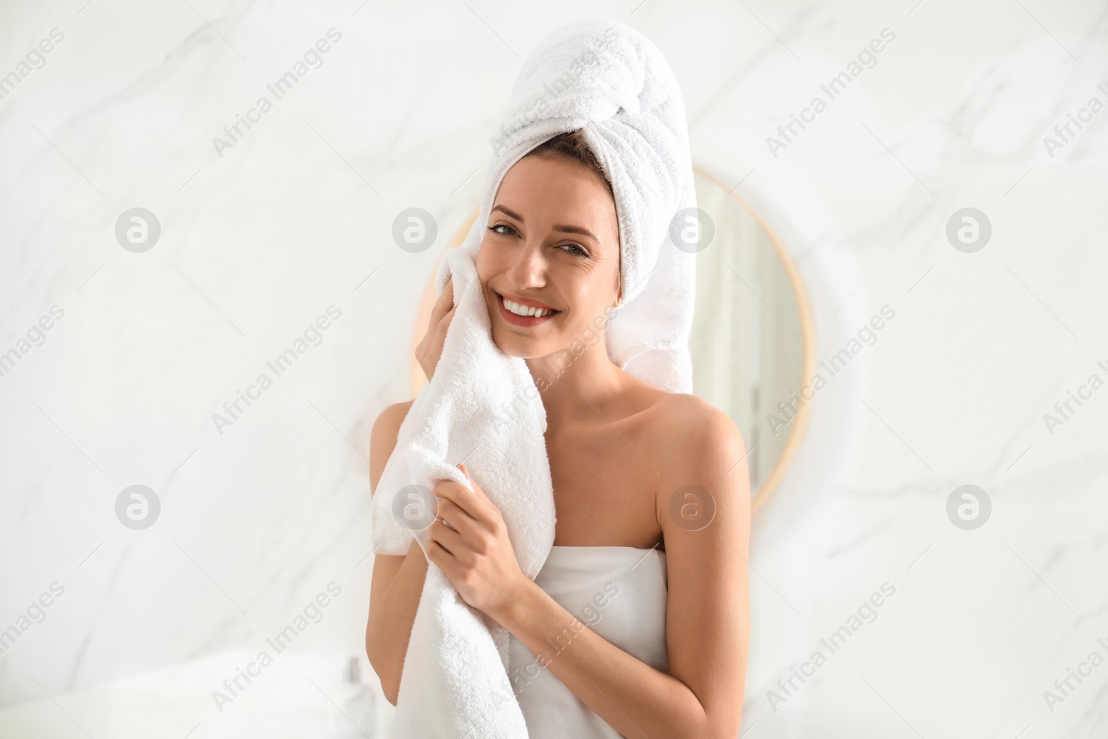 Photo of Young woman wiping face with towel in bathroom