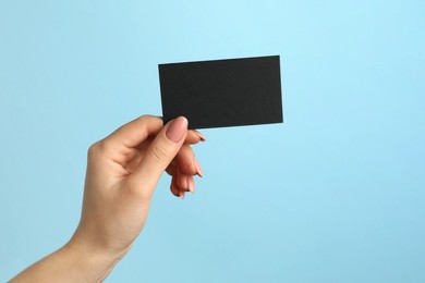 Photo of Woman with blank black business card on light blue background, closeup. Mockup for design