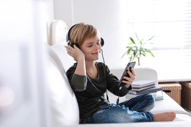 Cute little boy with headphones and smartphone listening to audiobook at home