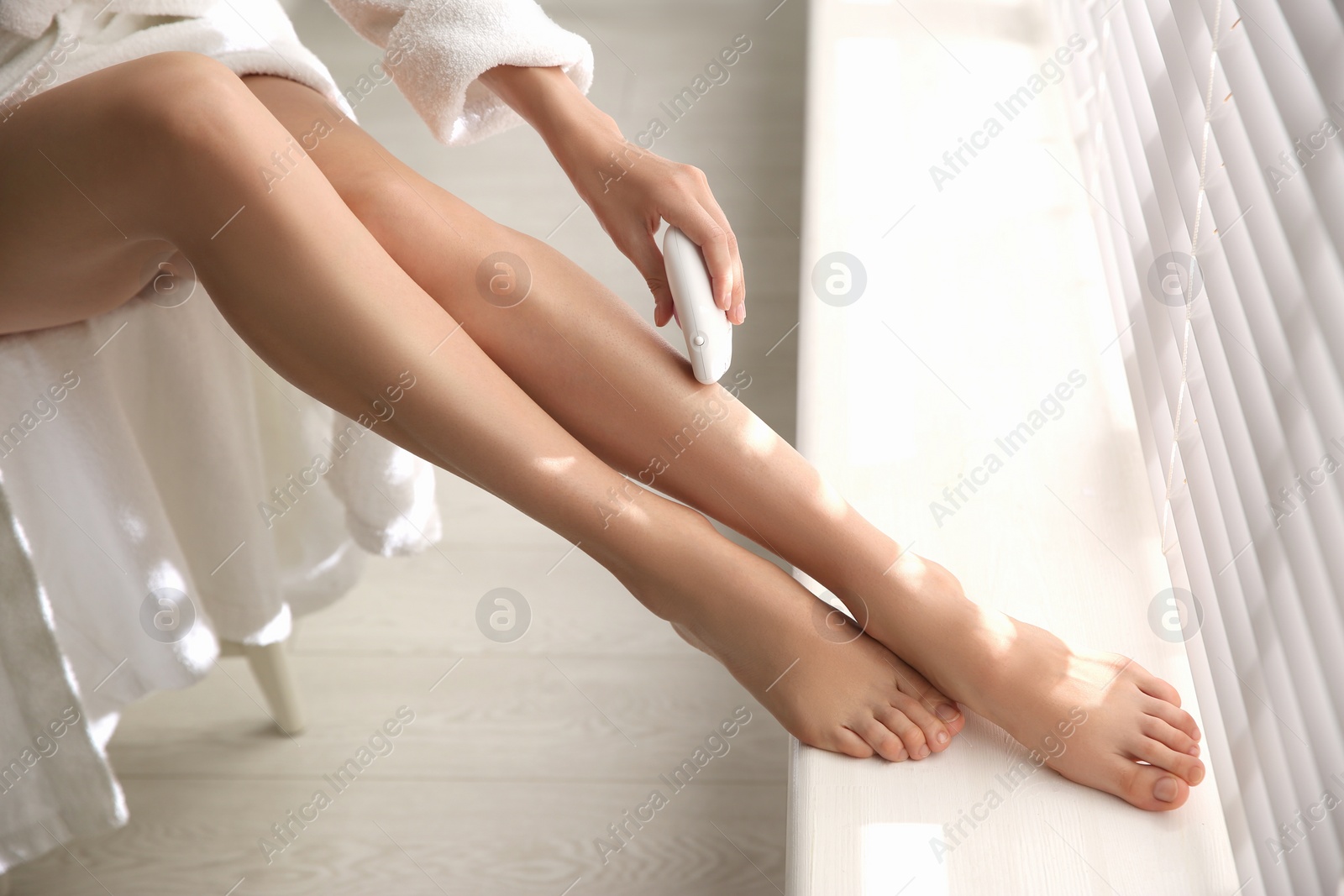 Photo of Woman doing leg epilation procedure near window indoors, closeup