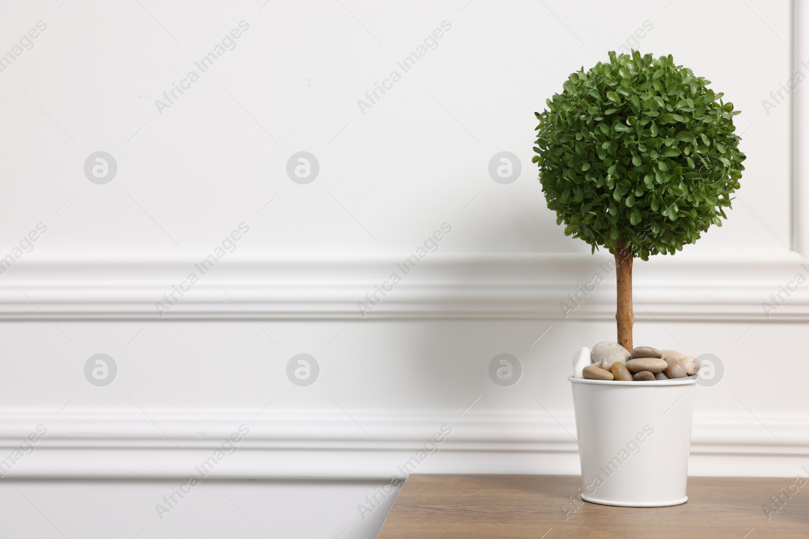 Photo of Green artificial plant in pot on wooden table near white wall, space for text