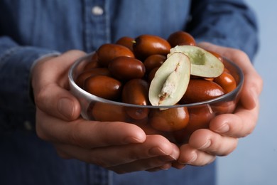 Photo of Woman holding glass bowl with fresh Ziziphus jujuba fruits on light background, closeup