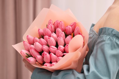 Photo of Woman holding bouquet of pink tulips indoors, closeup