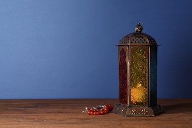 Photo of Muslim lamp with candle and misbaha on wooden table. Fanous as Ramadan symbol