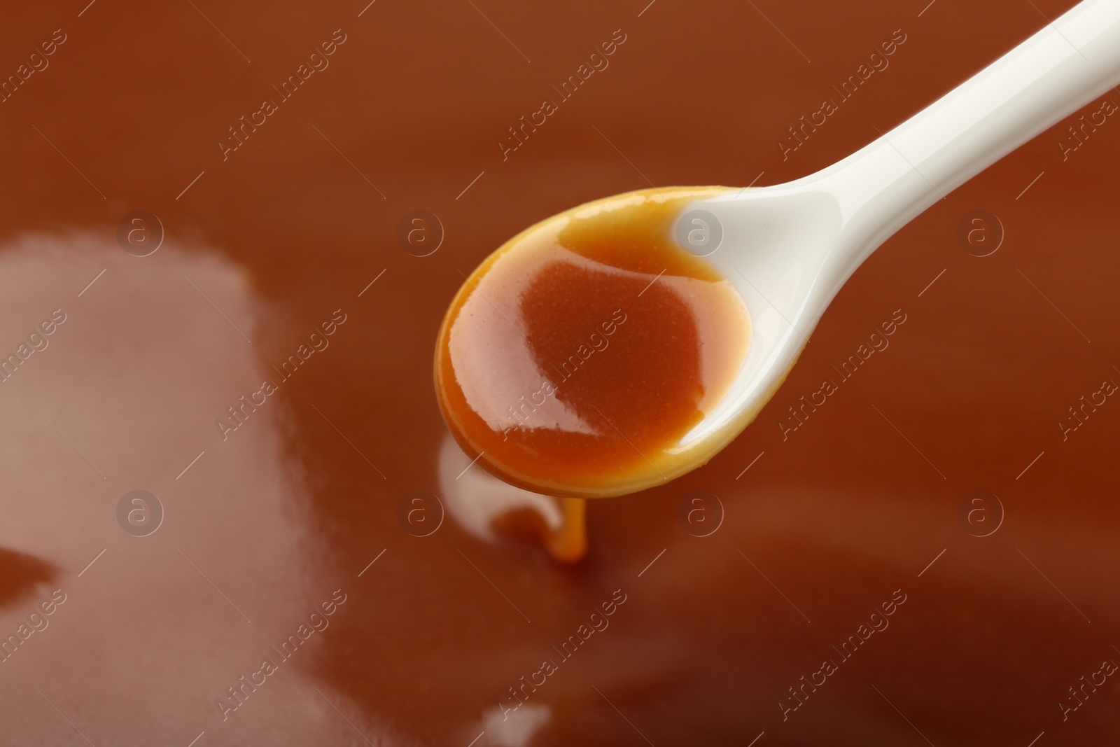 Photo of Taking tasty salted caramel with spoon, closeup. Space for text