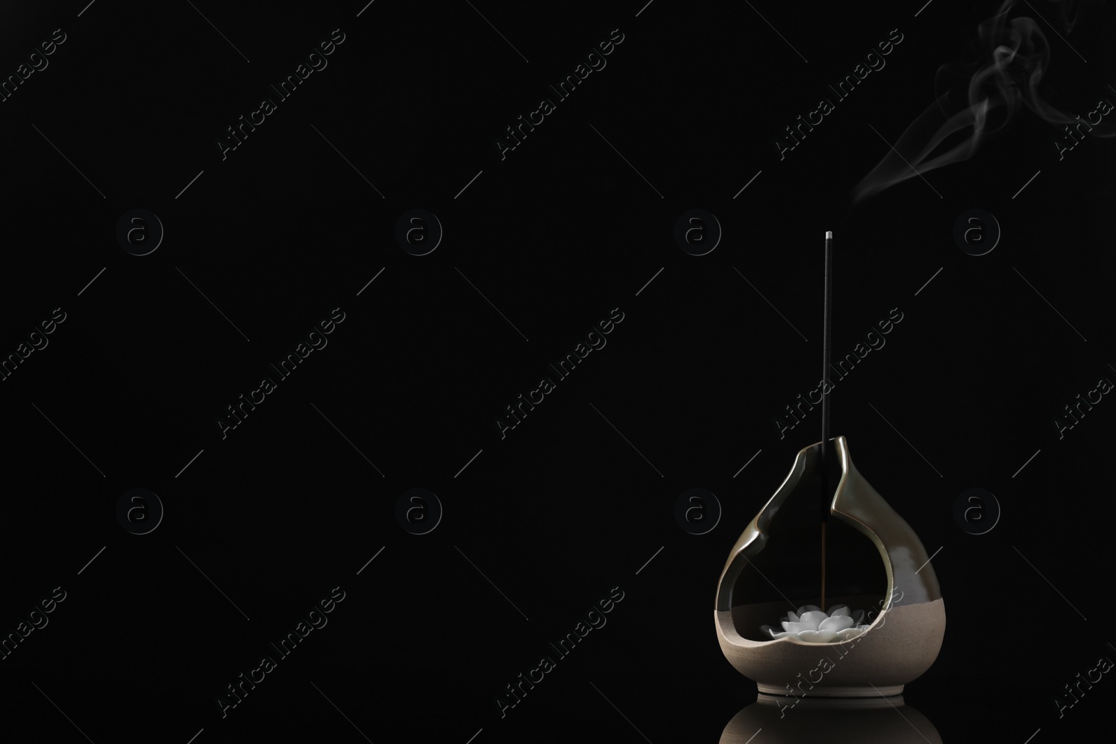 Photo of Incense stick smoldering in holder with lotus flower on black background. Space for text