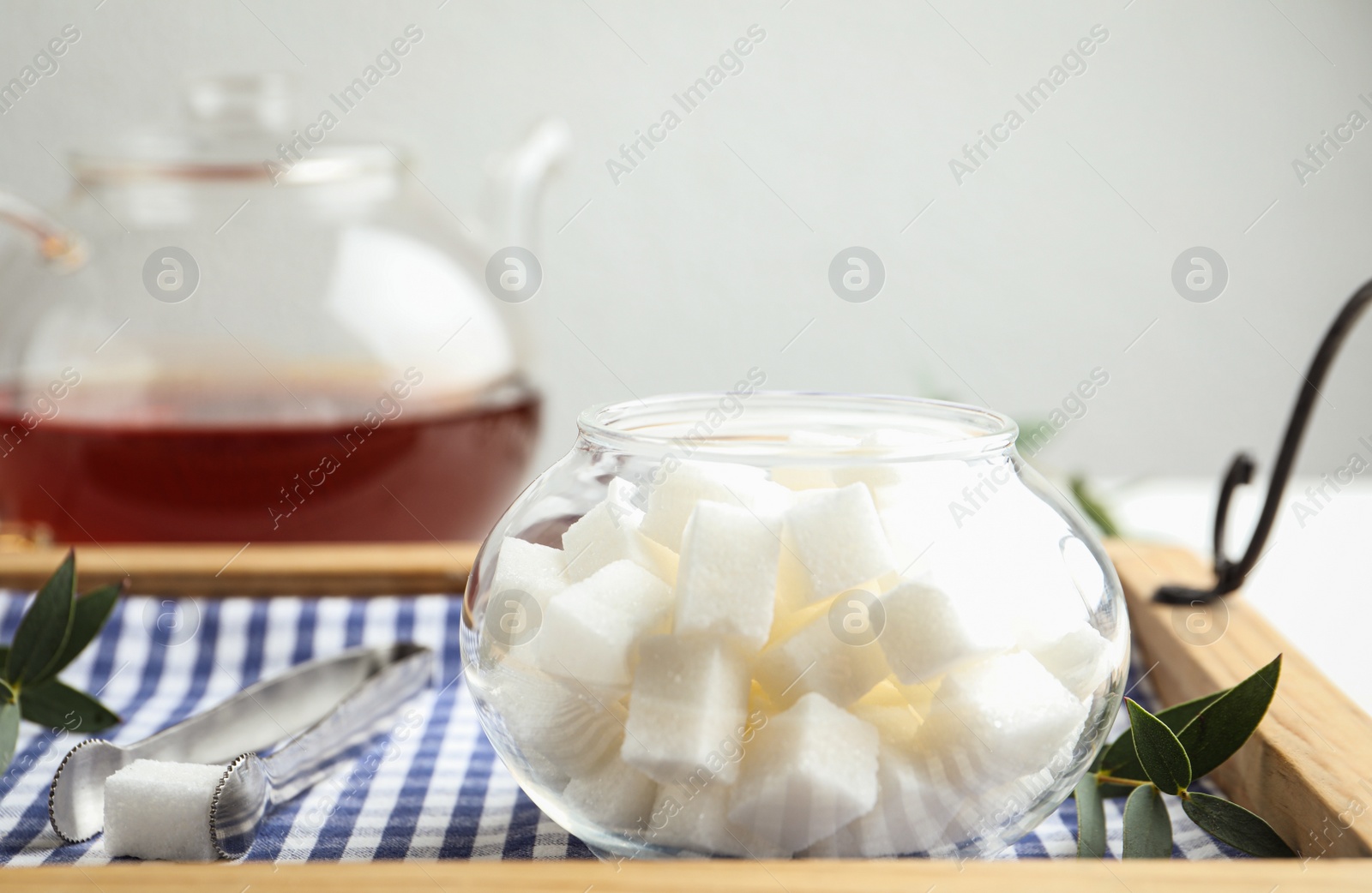 Photo of Refined sugar cubes in glass bowl and tongs on wooden tray