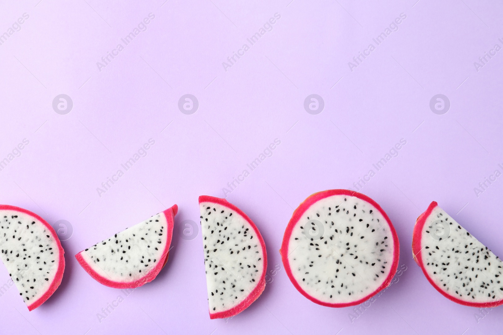 Photo of Slices of delicious dragon fruit (pitahaya) on violet background, flat lay. Space for text