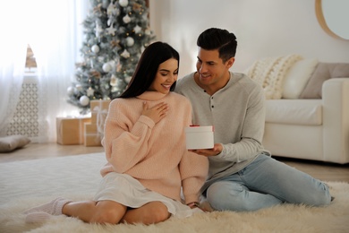 Photo of Boyfriend giving Christmas gift box to his girlfriend in living room