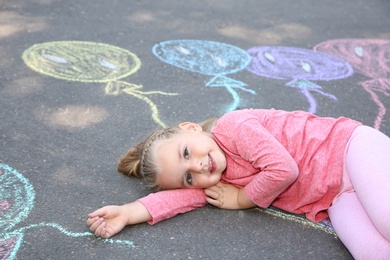 Photo of Little child lying near chalk drawing of balloons on asphalt