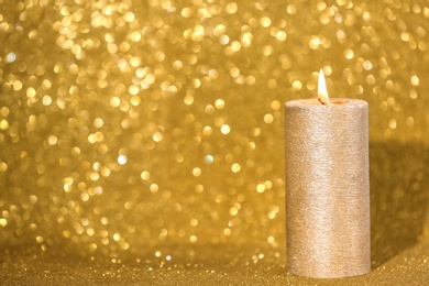 Photo of Burning candle on gold shining background, space for text