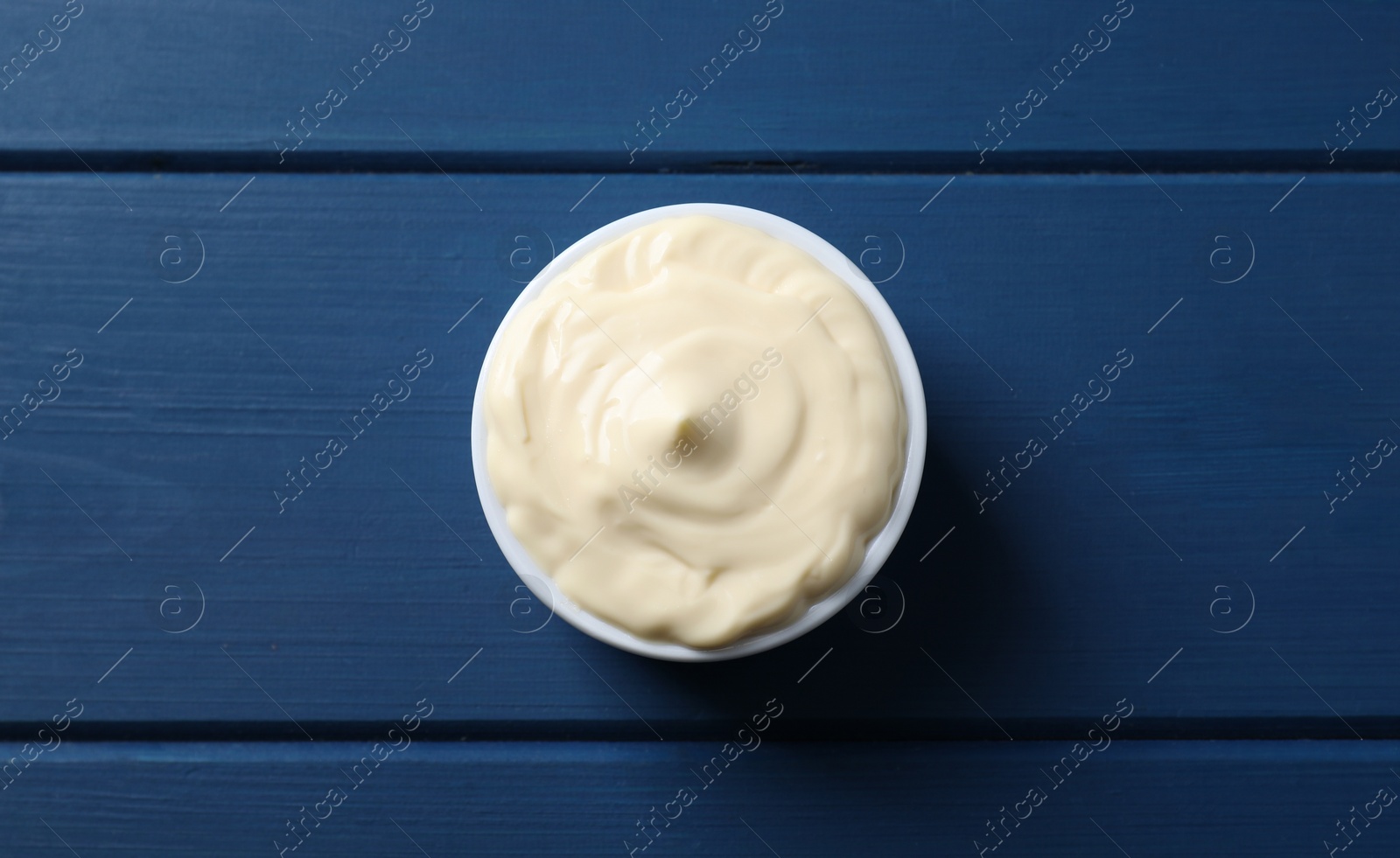 Photo of Tasty mayonnaise in bowl on blue wooden table, top view