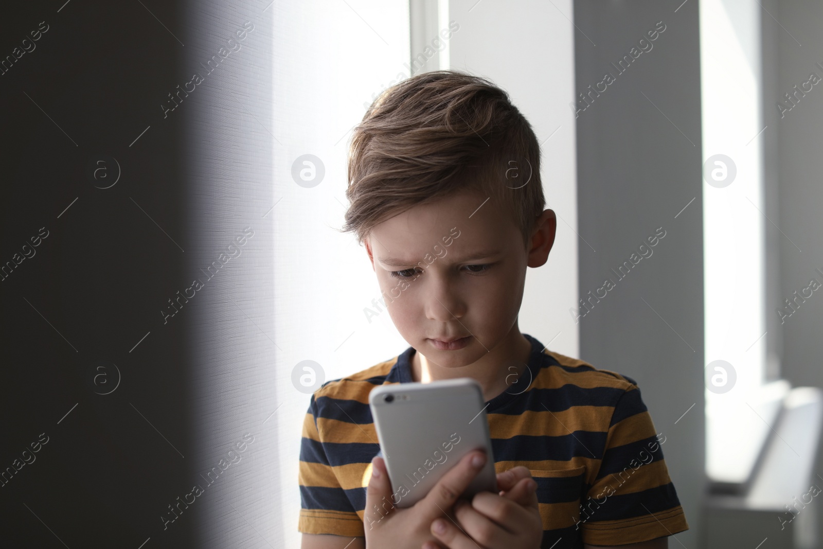 Photo of Sad little child with smartphone indoors. Danger of internet