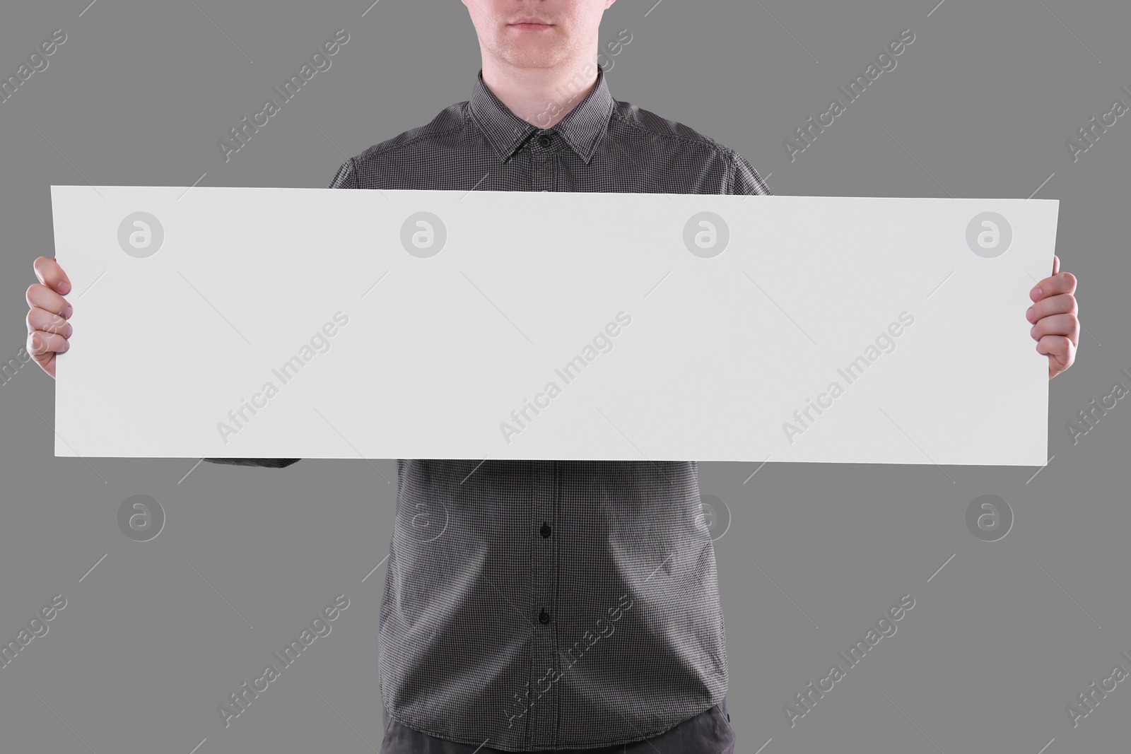 Photo of Man holding sheet of paper on grey background, closeup. Mockup for design