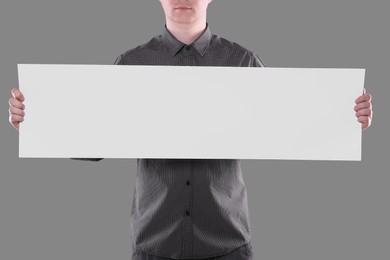 Man holding sheet of paper on grey background, closeup. Mockup for design