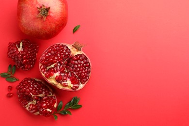 Photo of Fresh pomegranates and green leaves on red background, flat lay. Space for text