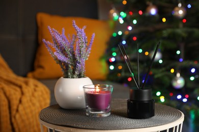 Photo of Aromatic reed air freshener, lavender and candle on side table in cozy room