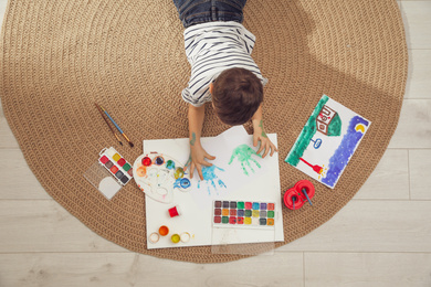 Photo of Little child painting on floor at home, top view