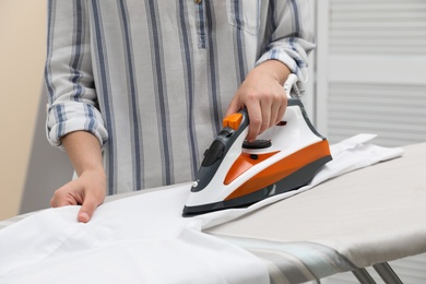 Woman ironing clean shirt on board against color background, closeup. Laundry day