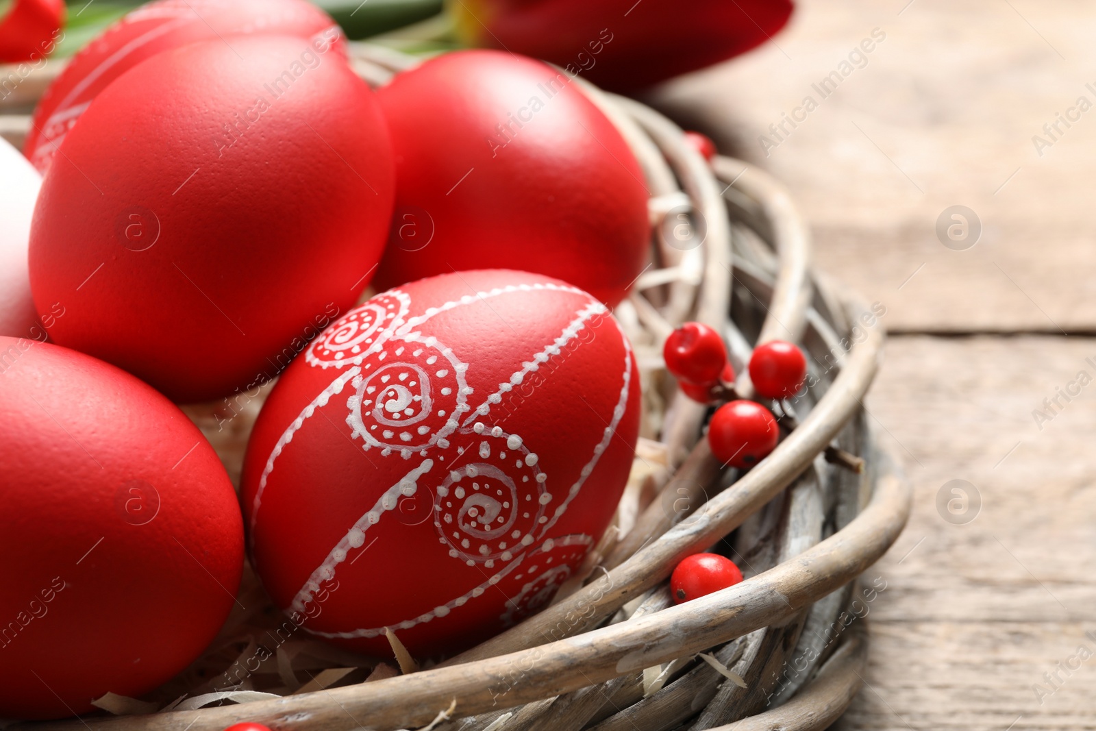 Photo of Wicker nest with painted Easter eggs on table, closeup