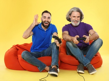 Photo of Mature man and guy playing video games with controllers on color background