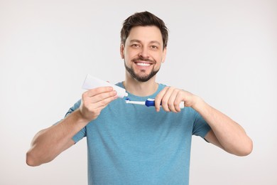 Photo of Happy man squeezing toothpaste from tube onto toothbrush on white background