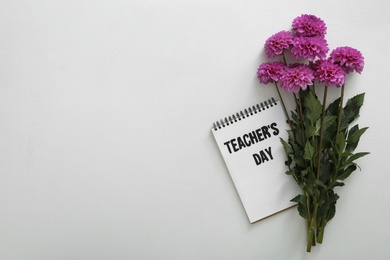 Photo of Beautiful flowers and notebook with words TEACHER'S DAY on white background, flat lay. Space for text