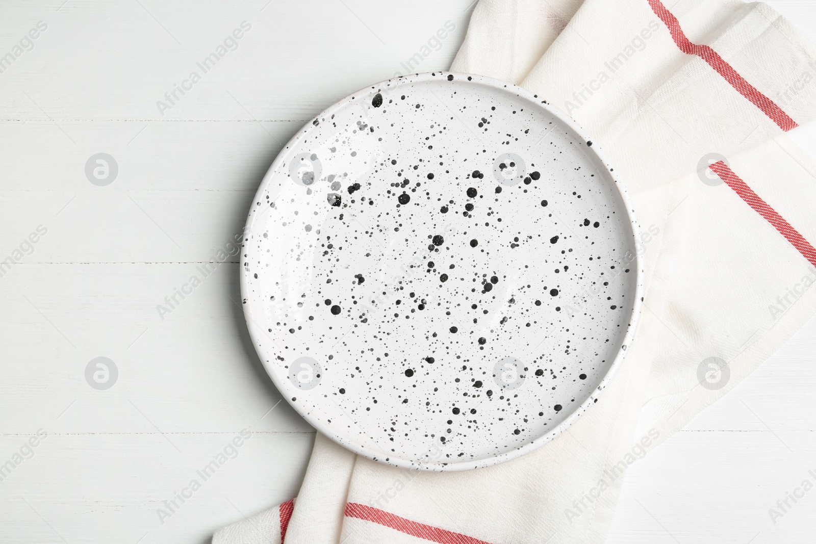 Photo of Empty patterned plate and fabric on white wooden table, flat lay