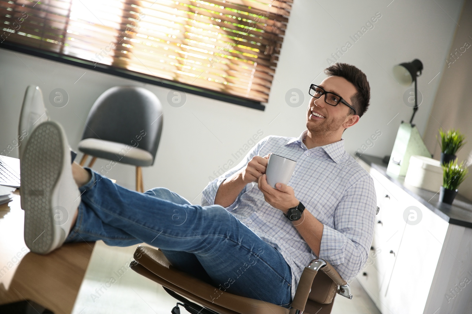 Photo of Young man with cup of drink relaxing at workplace