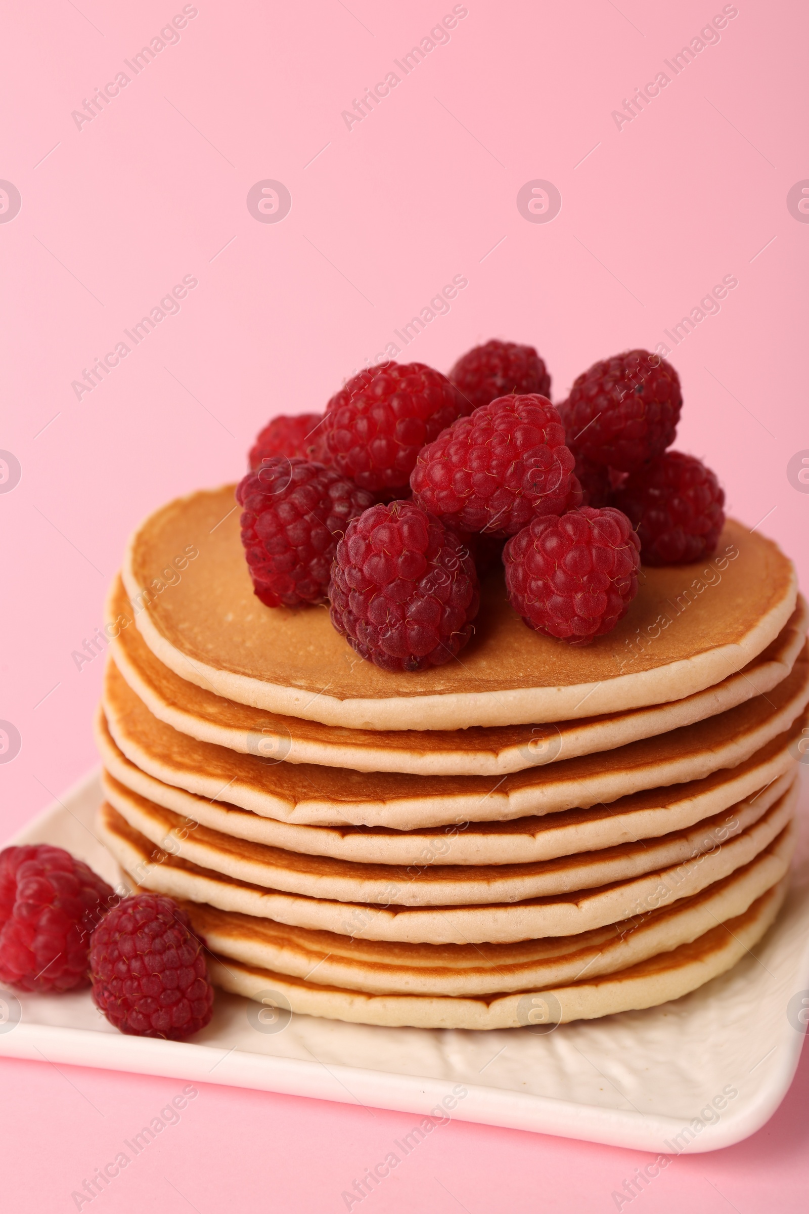 Photo of Stack of tasty pancakes with raspberries on pink background, closeup