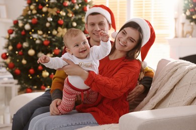 Happy couple with cute baby on sofa in room decorated for Christmas