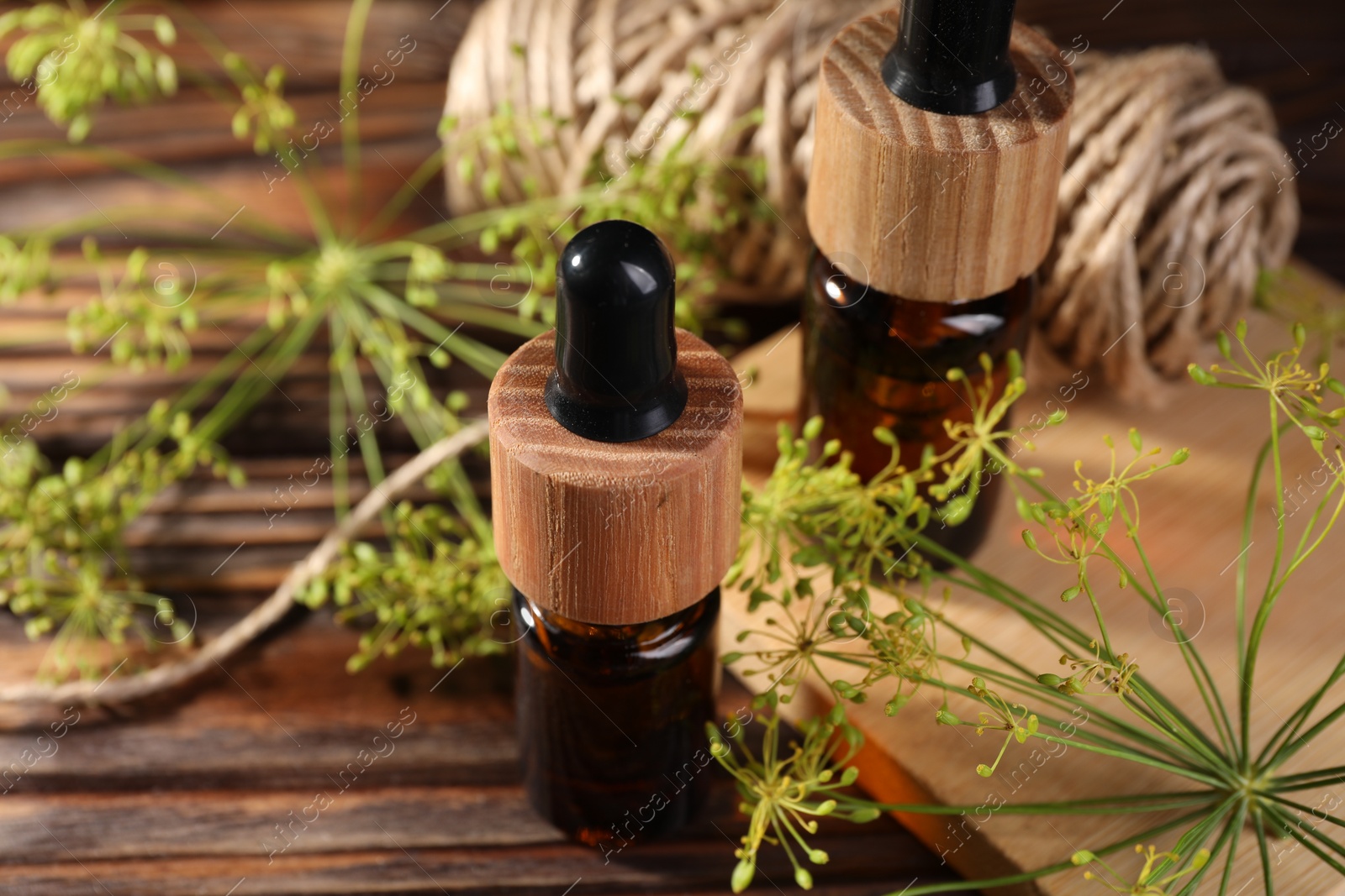 Photo of Bottle of essential oil, fresh dill and twine on wooden table, closeup