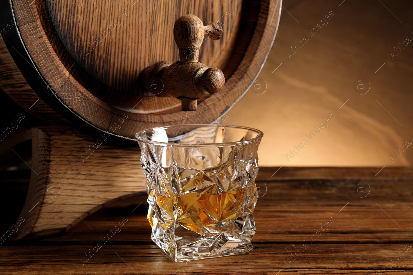 Photo of Glass of whiskey and wooden barrel on table, closeup