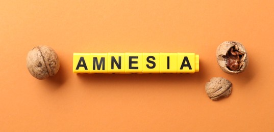 Photo of Word Amnesia made of yellow cubes and walnuts on orange background, flat lay