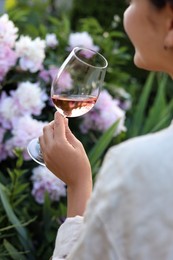 Woman with glass of rose wine in peony garden, closeup
