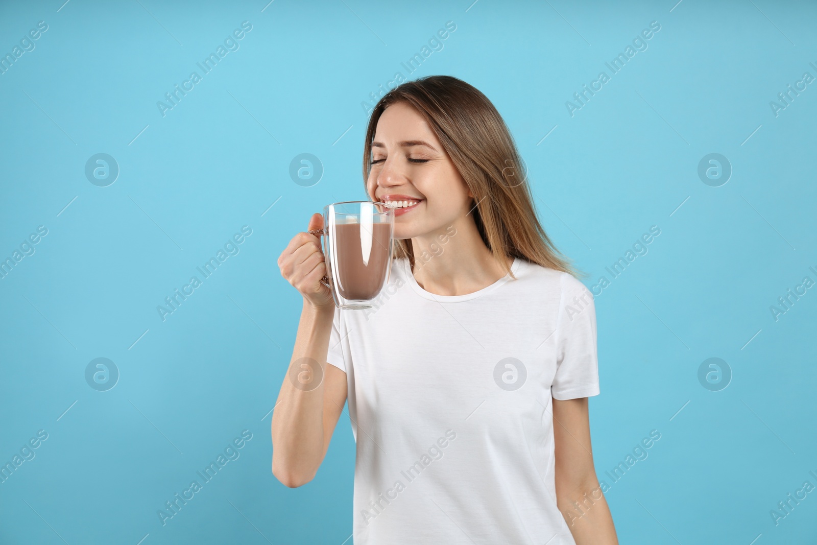Photo of Young woman drinking chocolate milk on light blue background