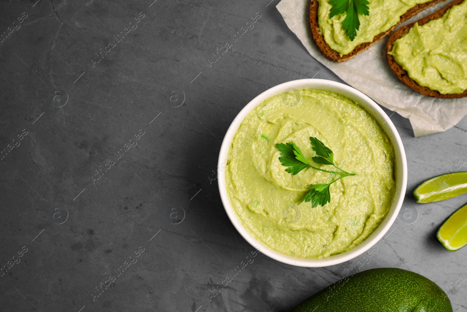 Photo of Flat lay composition with bowl of guacamole made of ripe avocados on grey table. Space for text