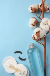 Bottle of makeup remover, cotton flowers, pads, swabs and false eyelashes on light blue background, flat lay. Space for text