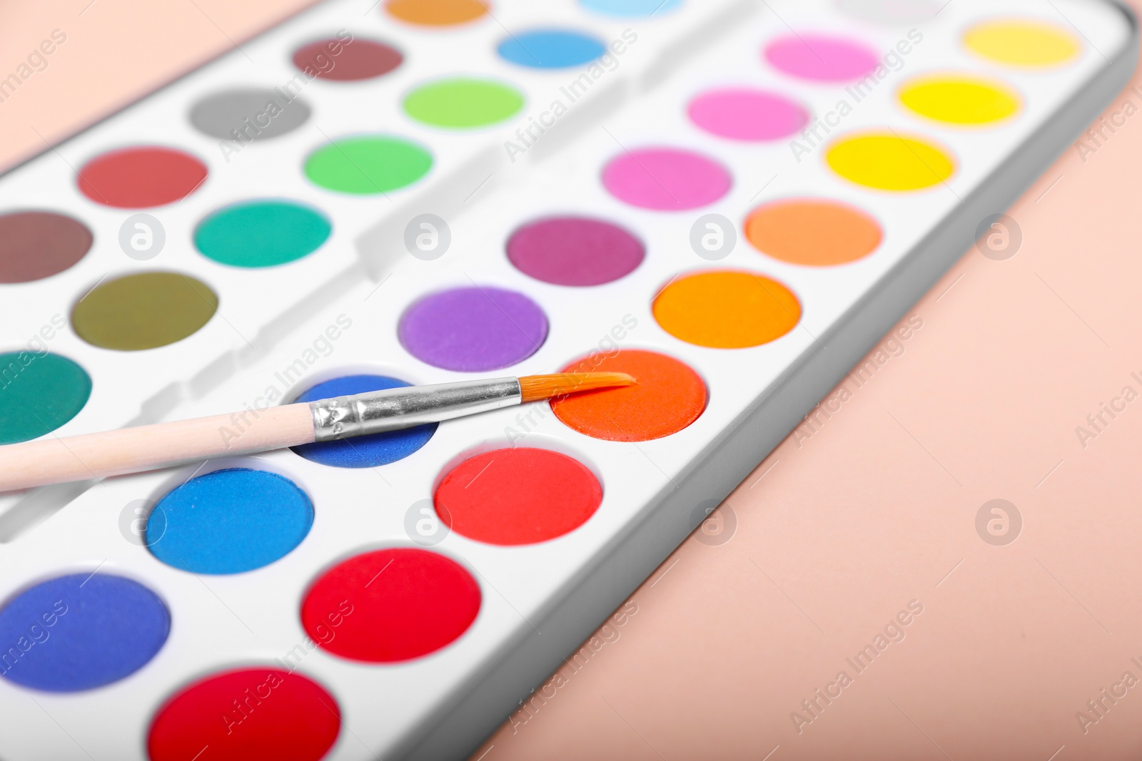 Photo of Watercolor palette with brush on beige background, closeup