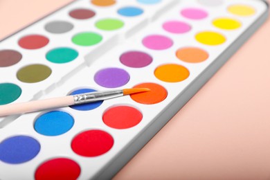 Photo of Watercolor palette with brush on beige background, closeup