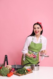 Photo of Young housewife cooking at white table on pink background. Space for text