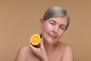 Photo of Beautiful woman with half of orange rich in vitamin C on beige background