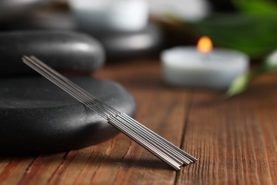 Photo of Acupuncture needles and spa stones on wooden table, closeup. Space for text