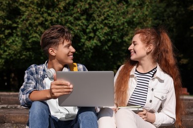 Photo of Happy young students studying with laptop together on steps in park