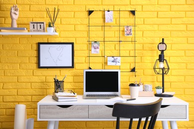 Stylish home office interior with comfortable workplace near yellow brick wall